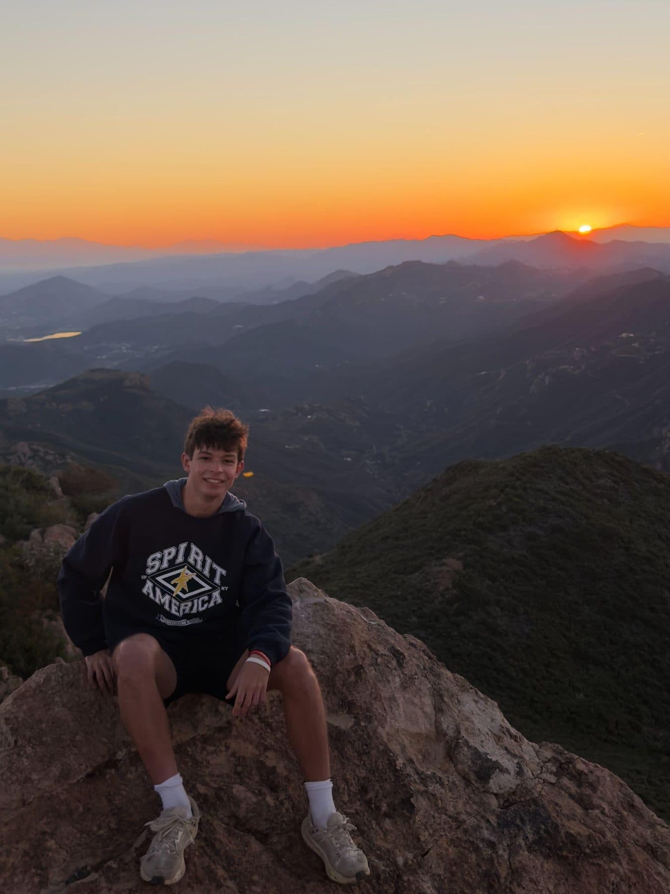 Jeffrey Lange sitting on a rock outcrop above a mountain range at sunset