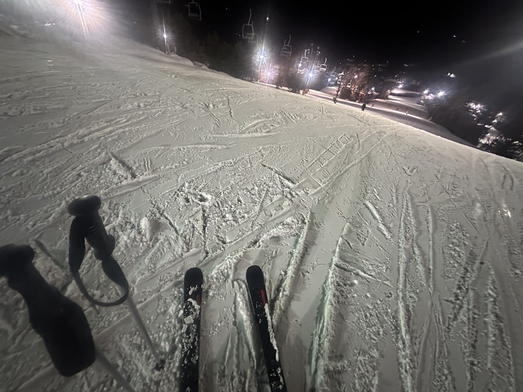 Skiing under the lights at night, looking down the piste toward the lodge