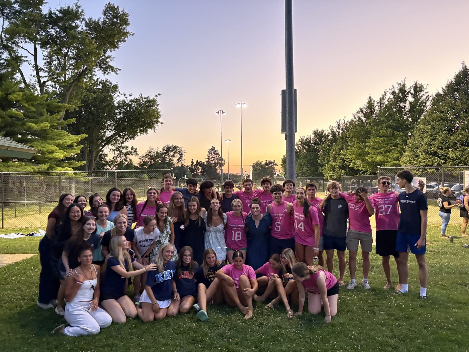 A large group of friends together on the field at sunset after a volleyball tournament