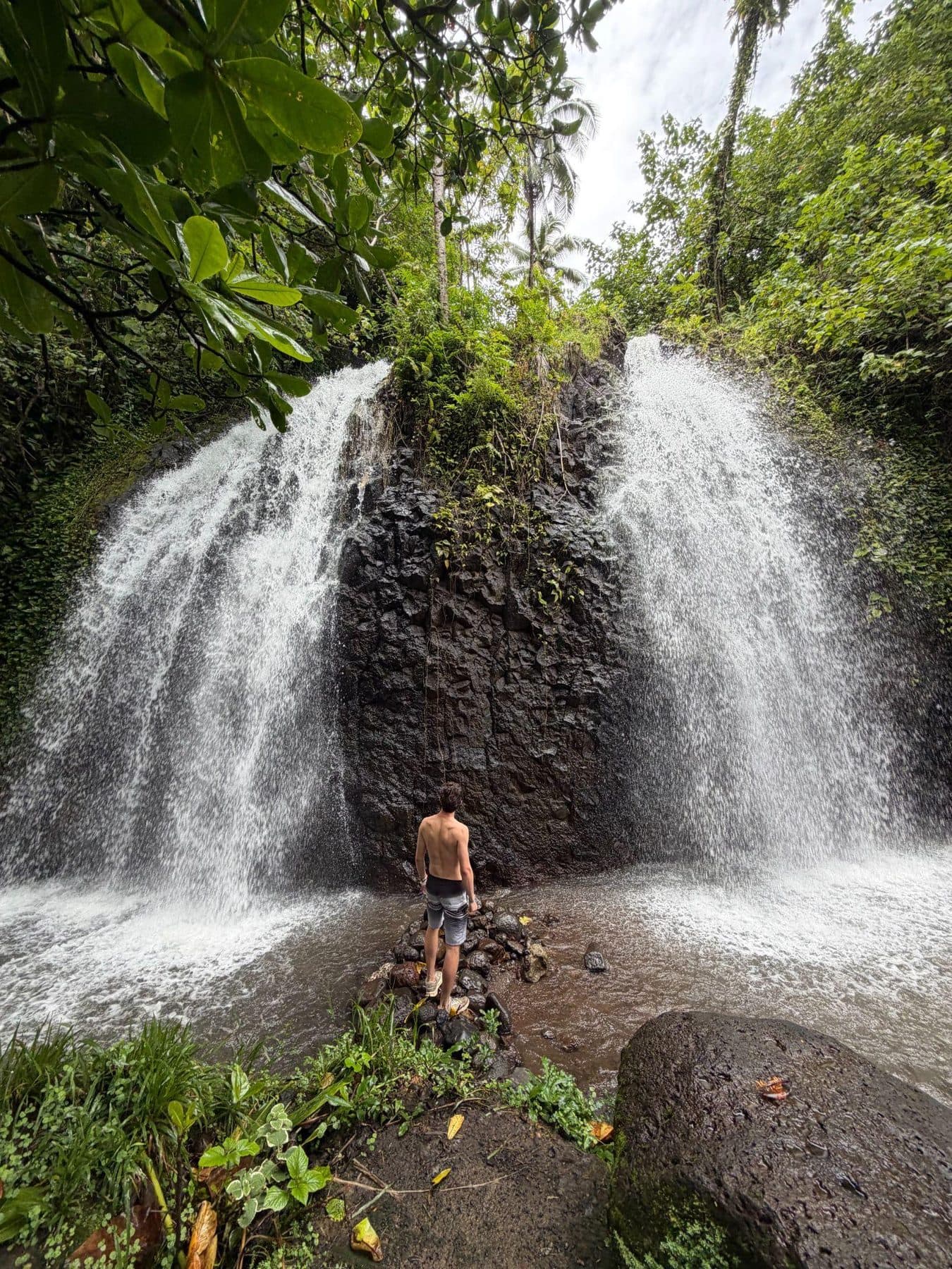 Jeffrey standing between two waterfalls in dense jungle